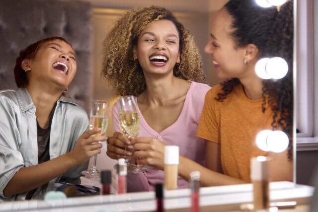 Group Of Female Friends At Home Putting On Make Up And Drinking Champagne